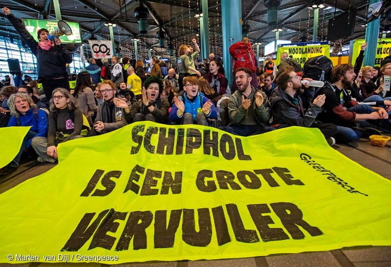 Demonstranten op Schiphol Plaza, met een banner waarop staat 'Schiphol is een grote vervuiler'. Schiphol moet krimpen.